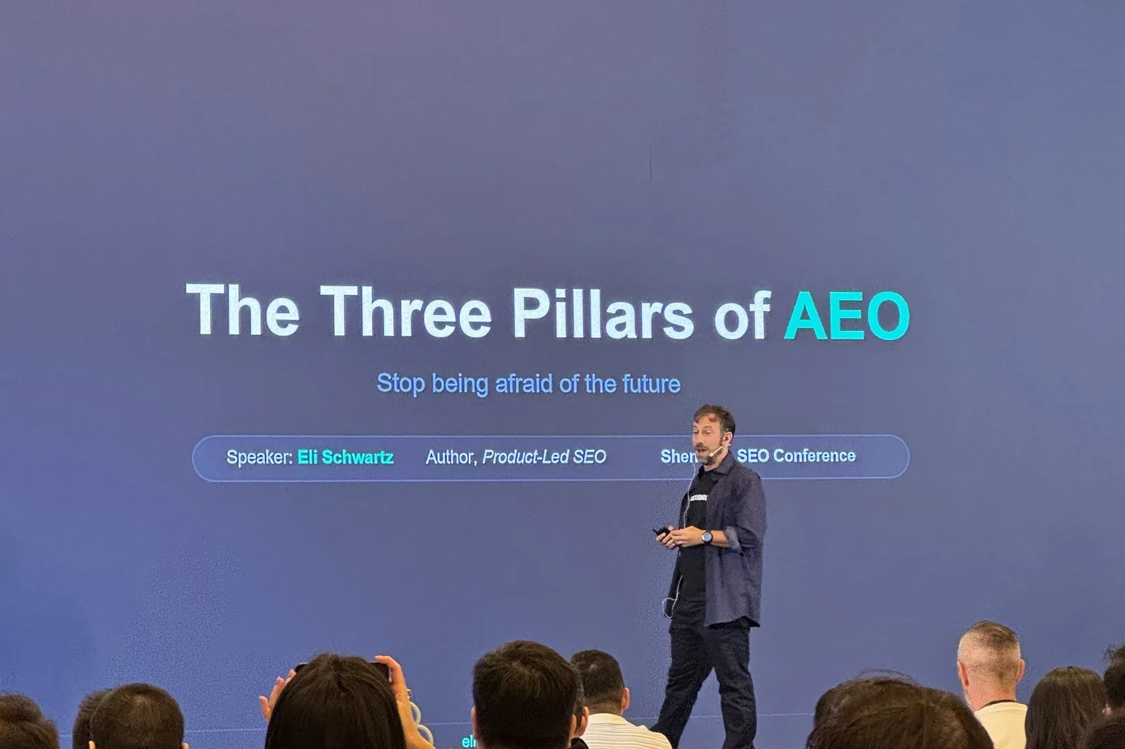 Eli Schwartz on stage with the slide The Three Pillars of AEO